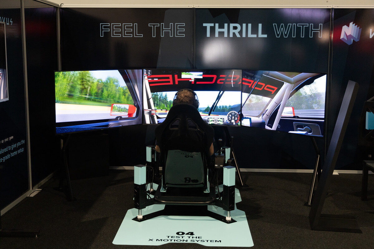 A man wearing a helmet and gloves sitting in a Novus high-end simulator with a curved screen displaying a racing game at the ADAC SimRacing Expo 2023.